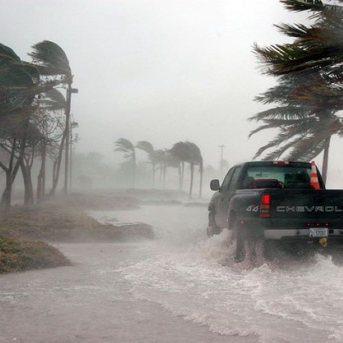 Key West. Hurricane force wind making landfall with black 4 wheel drive prickup truck driving along flooded windswept road.  With orange safety cone in the back. 