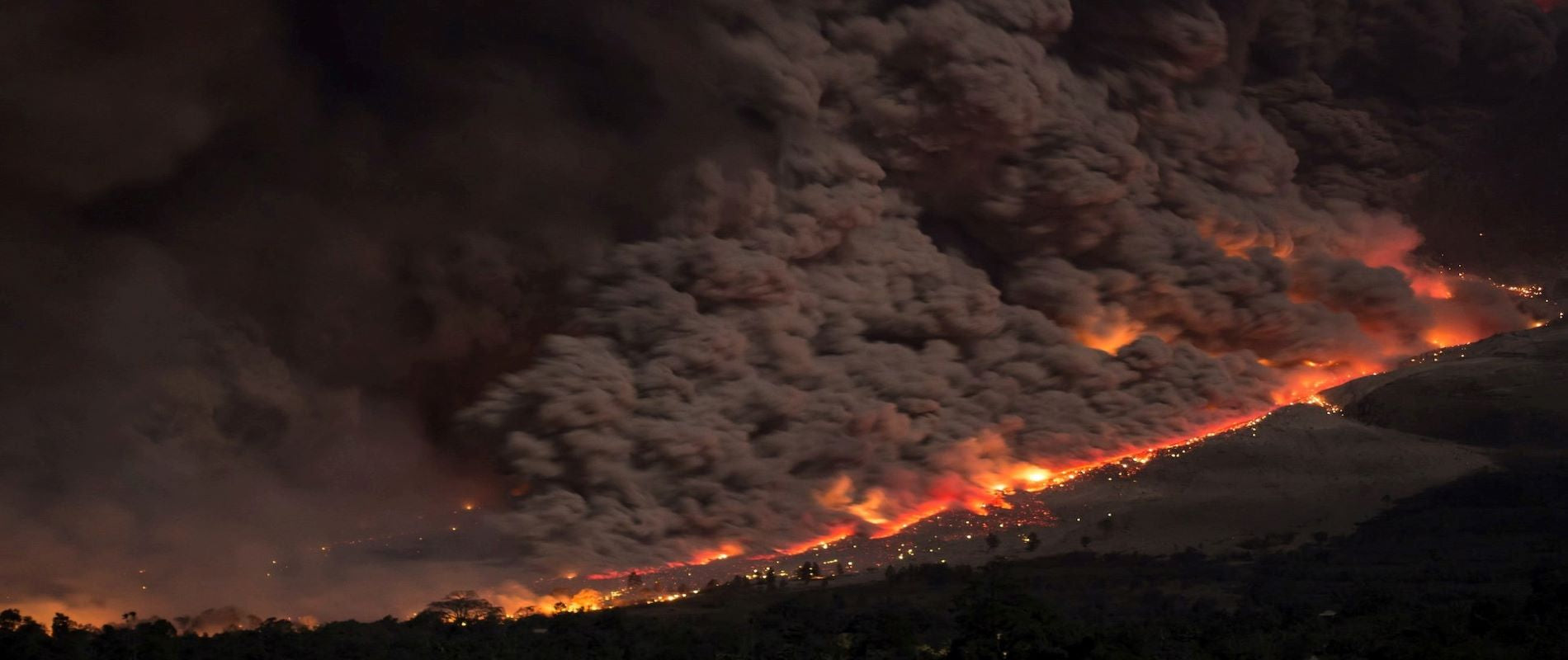 Natural Disaster Volcanic devastation. Orange hot lava flows over valley town with thick smoke and ash at night. 