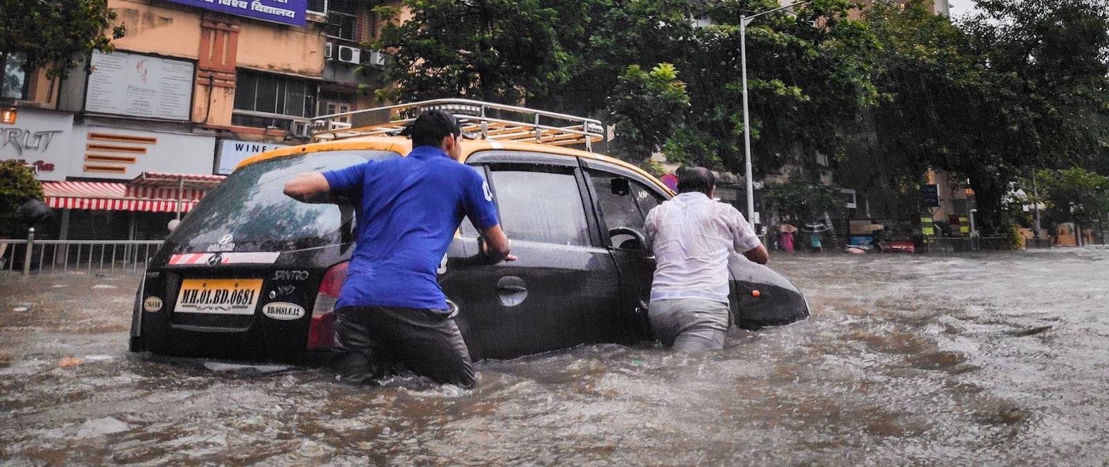 Storm serge widespread flooding - 2020 - two men pushing small car on city street through waist deep catestrophic water serge.