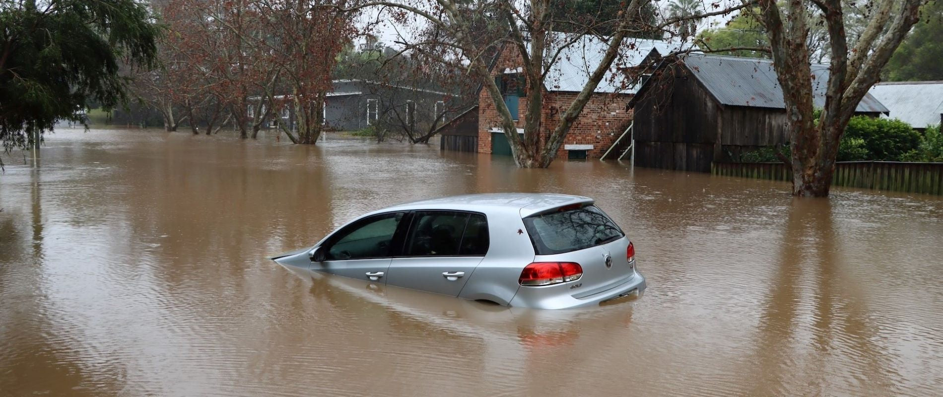 Atmosheric Natural Disaster. Residential mass flooding. Grey car floating in the street. 