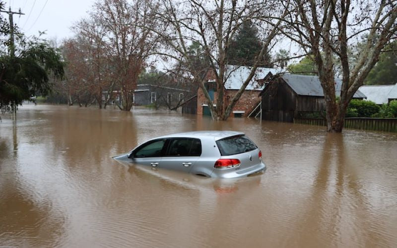 Atmosheric Natural Disaster. Residential mass flooding. Grey car floating in the street. 