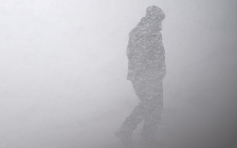 Person walking against the wind in a whiteout snowsquall snowstorm.